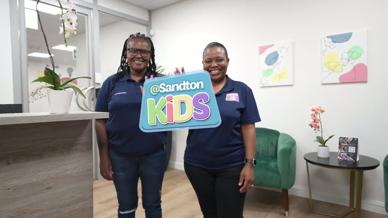 Two teachers smiling and holding the @Sandton Kids sign